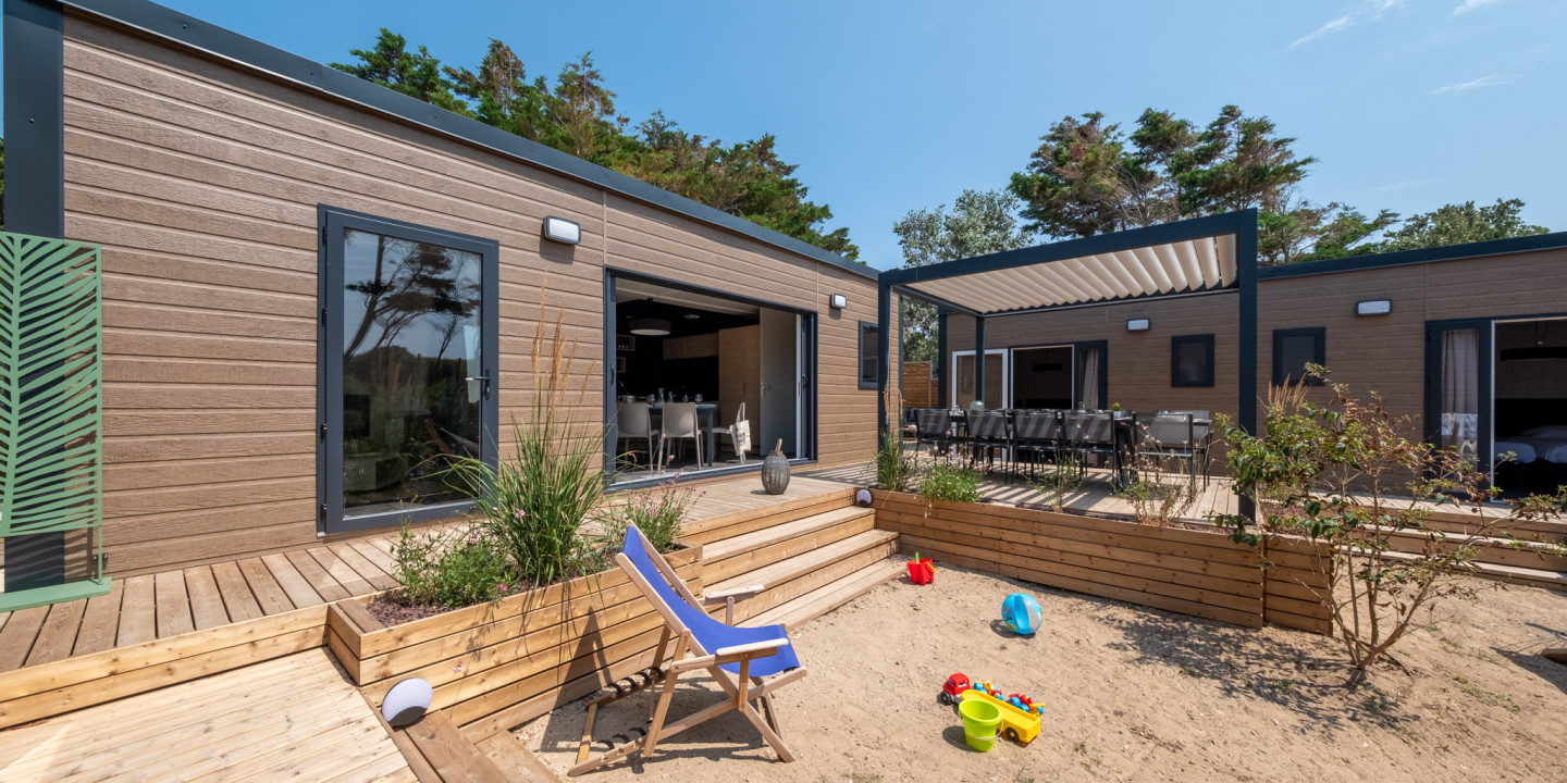 A small house featuring a deck and a patio, surrounded by greenery
