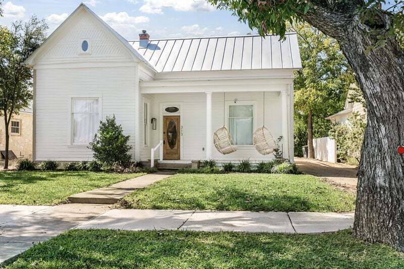 A white house featuring a metal roof and a welcoming porch