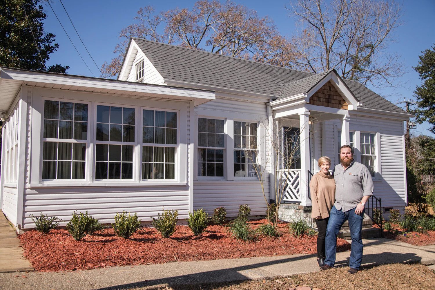 A man and woman stand together in front of a white house