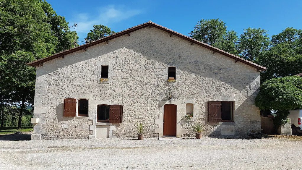 A stone house with wooden shutters and a gravel driveway