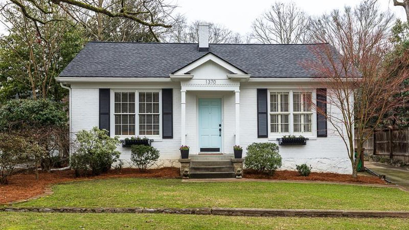 A small white house with blue trim surrounded by a well-kept front yard
